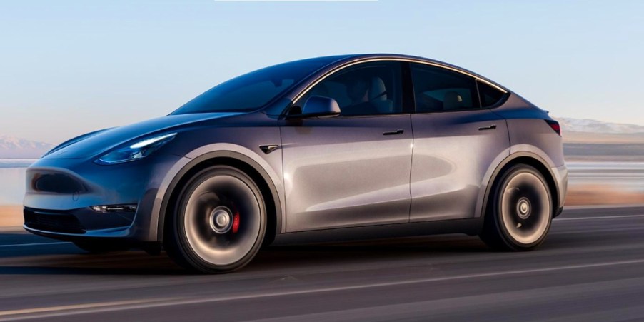 A gray Tesla Model Y small electric SUV is driving.