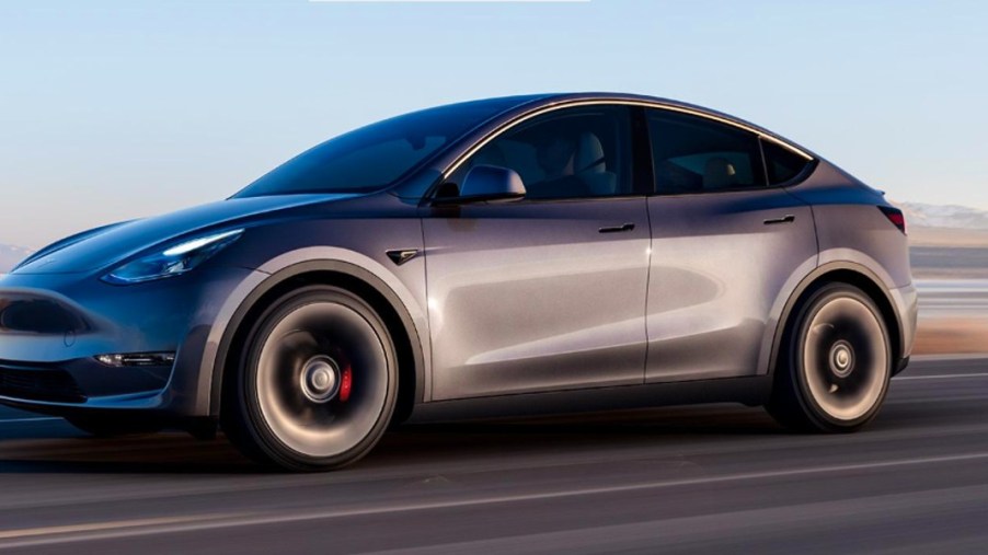 A gray Tesla Model Y small electric SUV is driving.