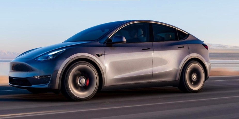 A gray 2023 Tesla Model Y small electric SUV is driving on the road. 