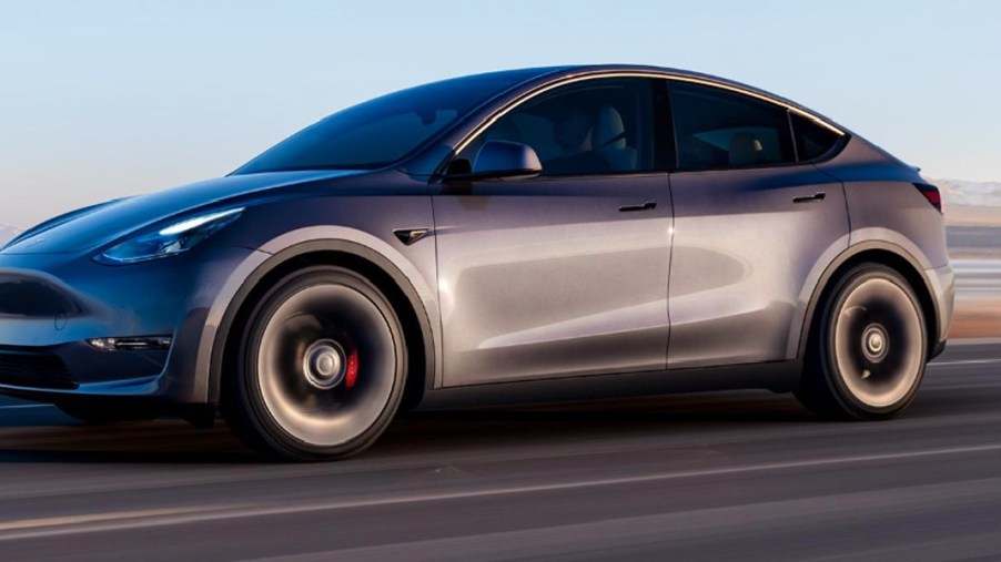 A gray 2023 Tesla Model Y small electric SUV is driving on the road.