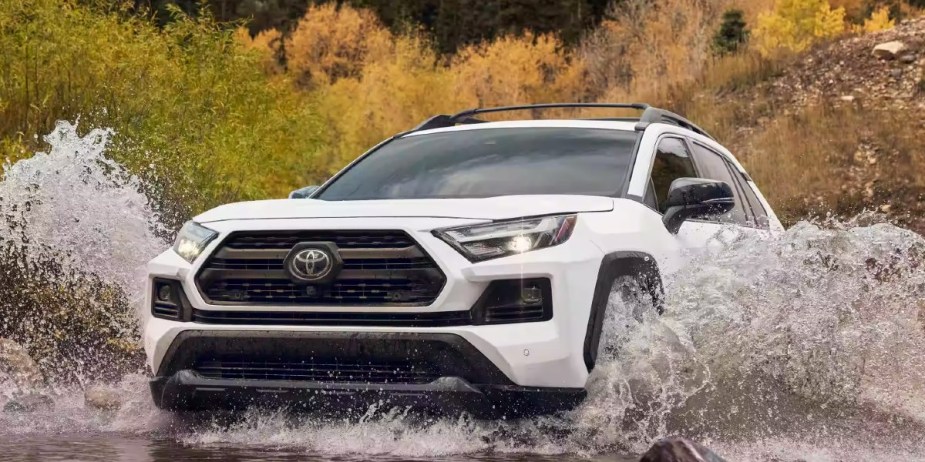 A white 2023 Toyota RAV4 small SUV is driving through the water. 