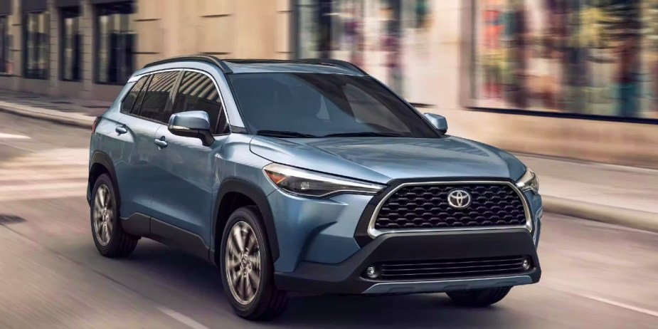 A blue 2023 Toyota Corolla Cross subcompact SUV is driving on the road.