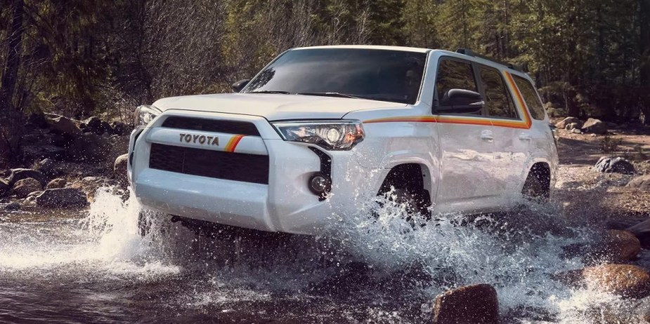 A white 2023 Toyota 4Runner midsize SUV is driving off-road through the water. 