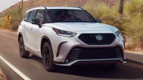 A white 2023 Toyota Highlander midsize SUV is driving on the road.