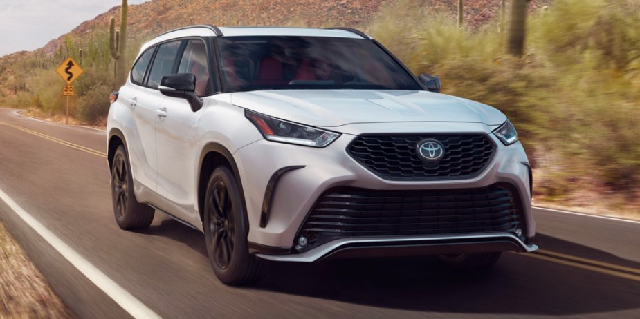 A white 2023 Toyota Highlander midsize SUV is driving on the road. 
