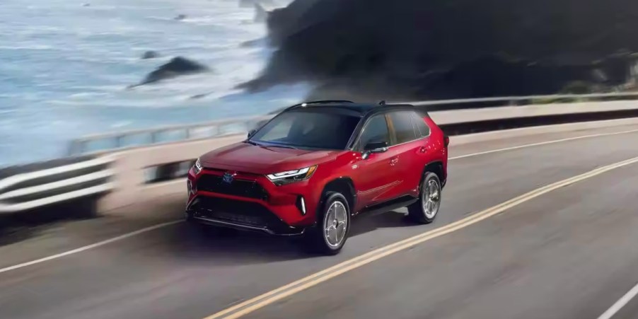 A red 2023 Toyota RAV4 Prime small plug-in hybrid SUV is driving near the ocean.