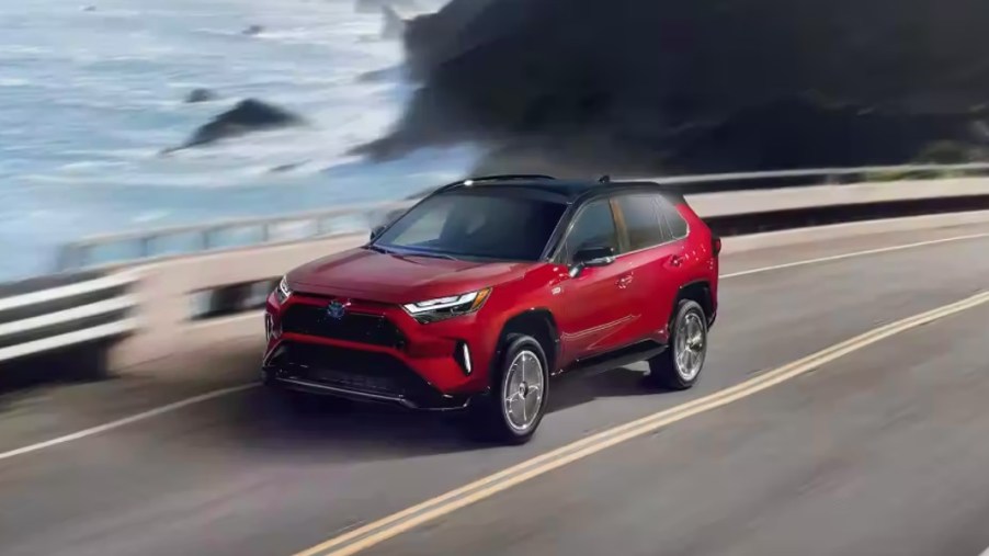 A red 2023 Toyota RAV4 Prime small plug-in hybrid SUV is driving near the ocean.