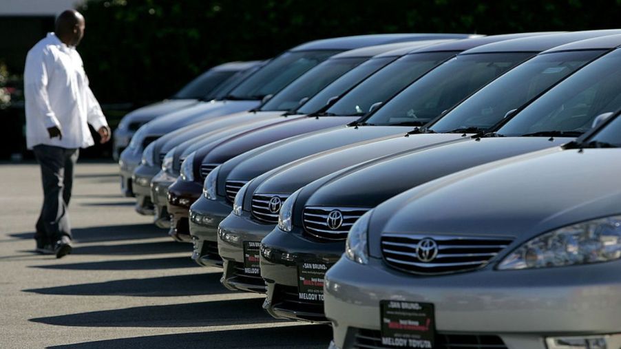 A man browses a row of used cars at a dealership.