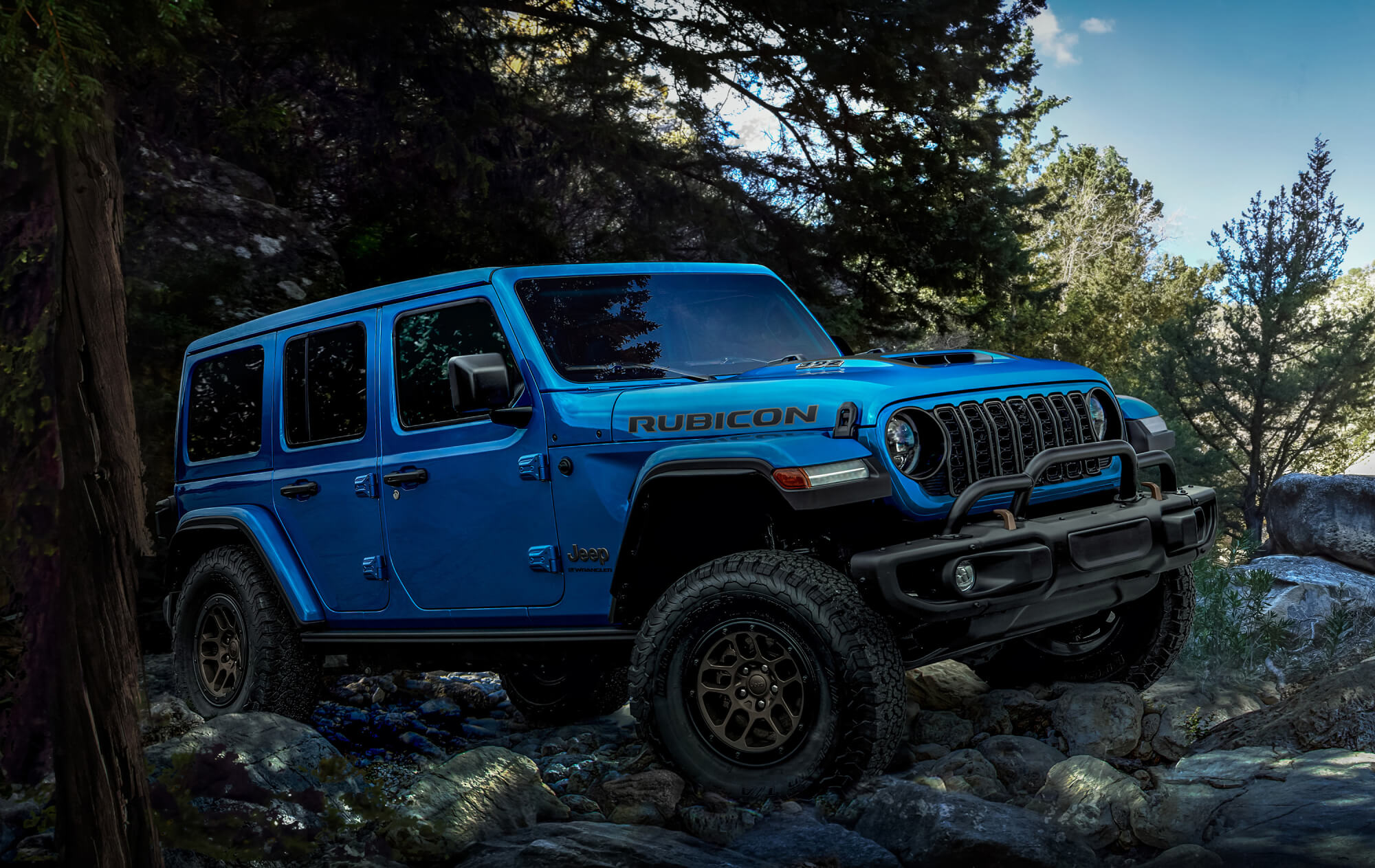 A blue Wrangler Rubicon 392 sitting atop rocks in a forest.