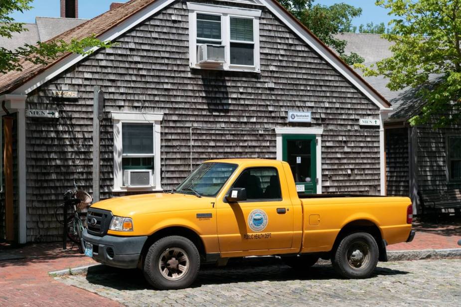 Yellow Ford Ranger compact pickup truck parked in front of a shingled house.