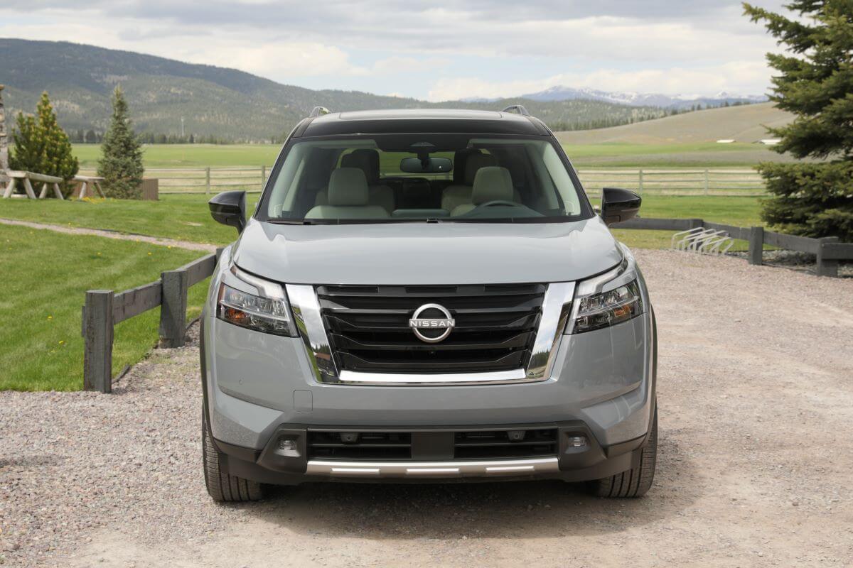 A dark-gray 2023 Nissan Pathfinder midsize SUV model parked on a gravel road framed by wood fencing