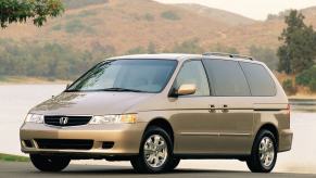 A gold/beige 2003 Honda Odyssey minivan model parked at the edge of a forest lake