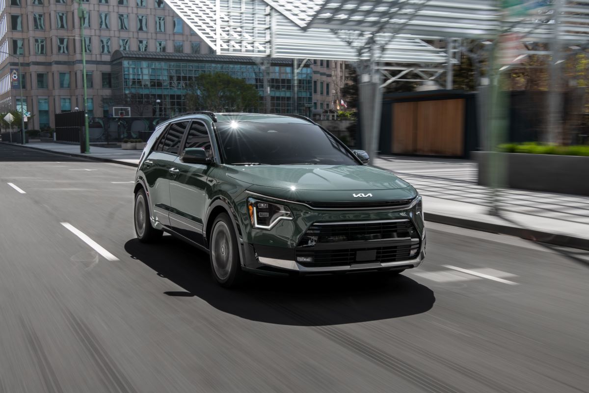 A green 2023 Kia Niro compact hybrid SUV model driving through an urban city
