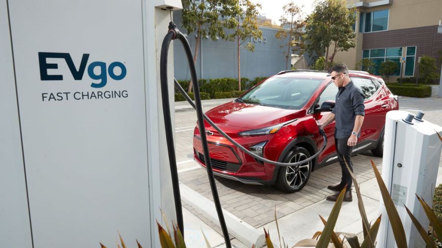 A red 2022 Chevy Bolt EUV electric compact SUV plugged into an EVgo fast charging station