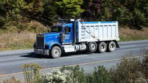 A blue semi, potentially using Jake Braking to slow it down, driving down a wooded area.