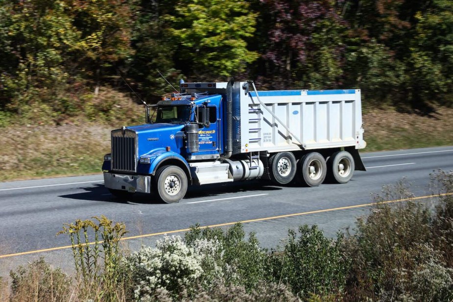 A blue semi, potentially using Jake Braking to slow it down, driving down a wooded area.