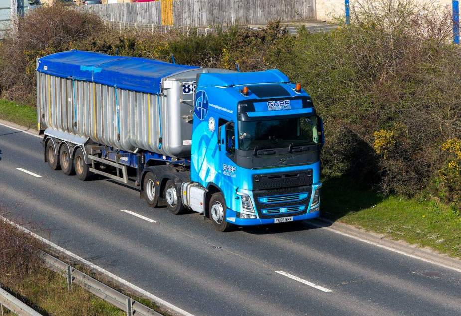 A blue semi-truck driving  down a highway, potentially using Jake Braking. 