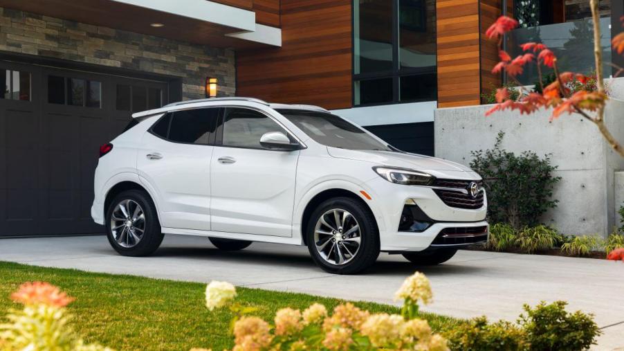 A white 2023 Buick Encore GX subcompact SUV model parked on a driveway of a luxury house near flowers
