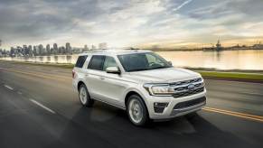A white 2023 Ford Expedition full-size SUV model driving on a highway near water