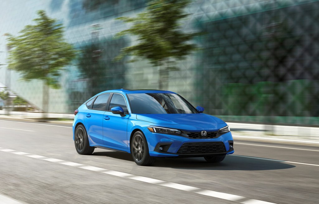 A bright blue 2022 or 2023 Honda Civic Sport Hatchback cruises city streets. 