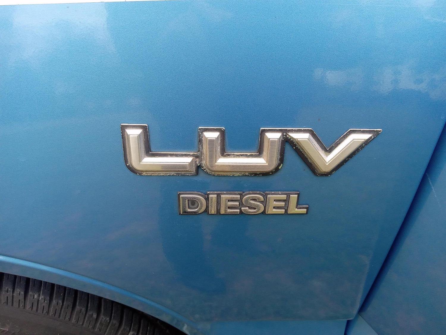 The LUV and Diesel badges on the blue front fender of a compact Chevrolet pickup truck built by Isuzu for 1982.