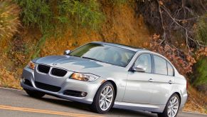 A used silver 2007 BMW 335i cruises around a hilltop.