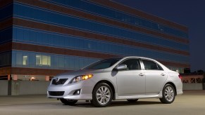 A used silver 2009 Toyota Corolla, which could have airbag and oil burning issues, poses next a high-rise building.