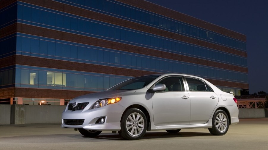 A used silver 2009 Toyota Corolla, which could have airbag and oil burning issues, poses next a high-rise building.