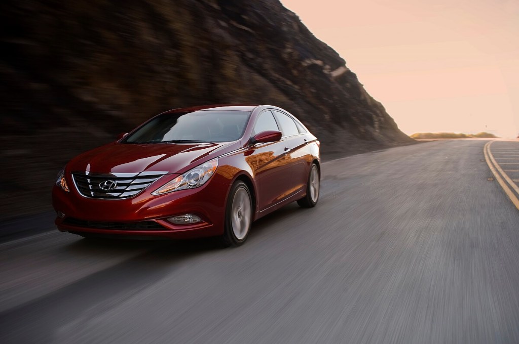 A red 2011 Hyundai Sonata model drives mountain roads.
