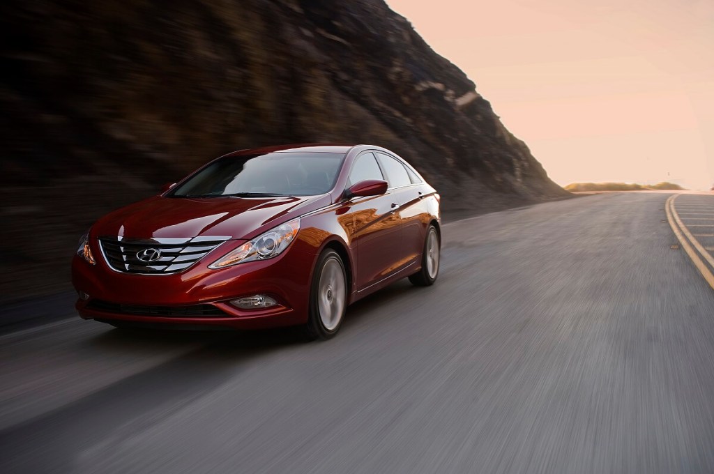 A red 2011 Hyundai Sonata model drives mountain roads. 