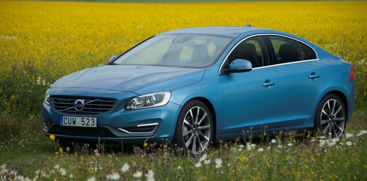 A blue 2014 Volvo S60 luxury sedan model parked in a field of grass amid yellow flowers