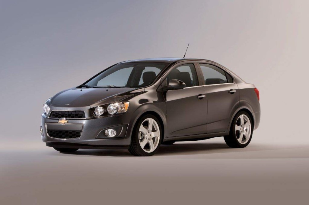 A grey 2015 Chevy Sonic parked in a blue and grey room. 
