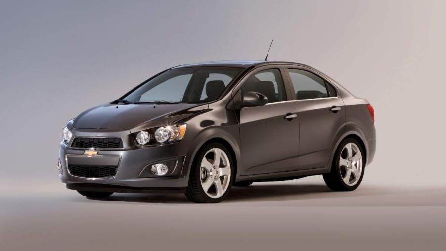 A grey 2015 Chevy Sonic parked in a blue and grey room.