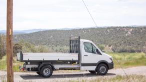 A shite Mercedes-Benz sprinter truck parked sideways on a dirt road, a ridge of mountains visible in the background.