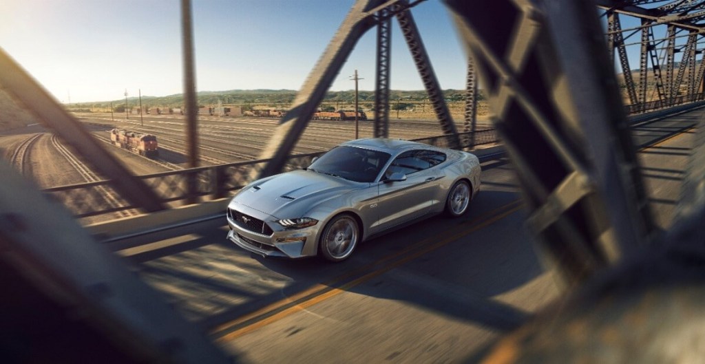 A silver 2018 Ford Mustang blasts across an urban bridge.