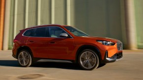 An orange 2023 BMW X1subcompact luxury SUV is driving.