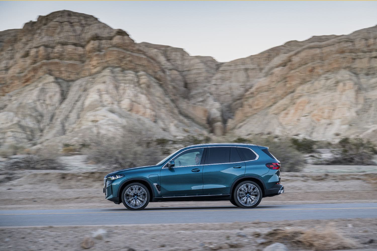 A blue 2023 BMW X5 driving down an open road.