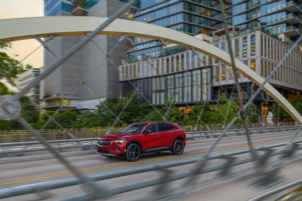 A red 2023 Buick Envision driving down the highway in a city with buildings in the background.