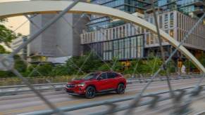 A red 2023 Buick Envision driving down the highway in a city with buildings in the background.