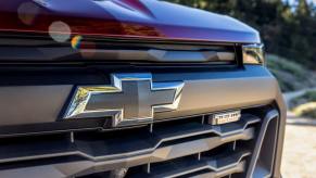 A closeup shot of the grille emblem and Trail Boss badging of a red 2023 Chevy Colorado Trail Boss