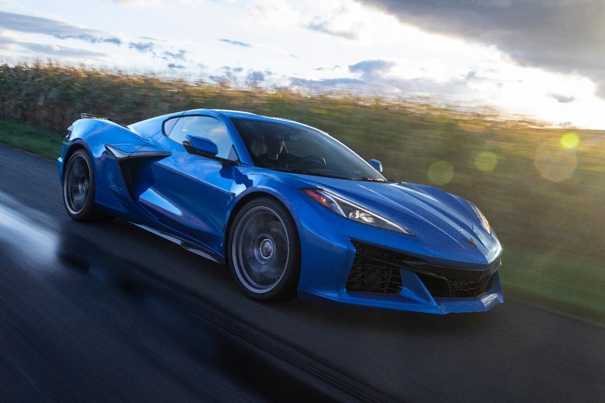 A bright blue Chevy Corvette Z06 supercar from the C8 generation blasts down a back road.