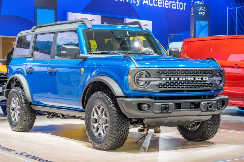 A blue Ford Bronco parked indoors against a blue background and white floor. 
