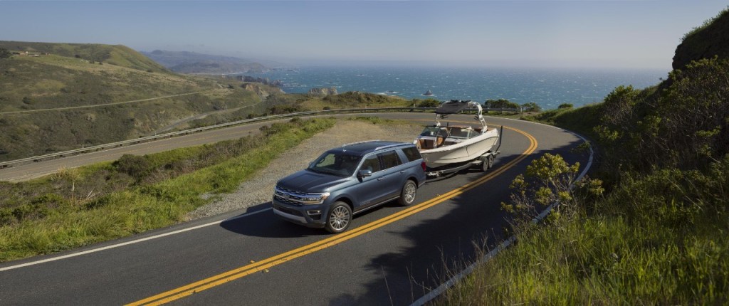 A new Ford Expedition tows a boat a tight corner with blue ocean in the background. The Expedition is an SUV alternative to Ford's pickup trucks. 