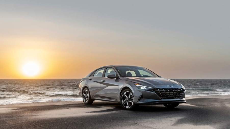 A grey 2023 Hyundai Elantra Hybrid parked in front of a sunset on a beach, one of the best small cars of 2023.