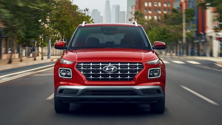 A red 2023 Hyundai Venue subcompact SUV is driving on the road.