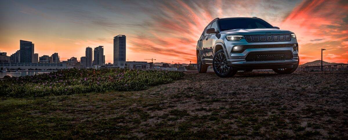A silver 2023 Jeep Compass with a sunset in the background and a city skyline.