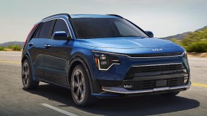 A blue 2023 Kia Niro Plug-In Hybrid subcompact PHEV SUV is driving on the road.