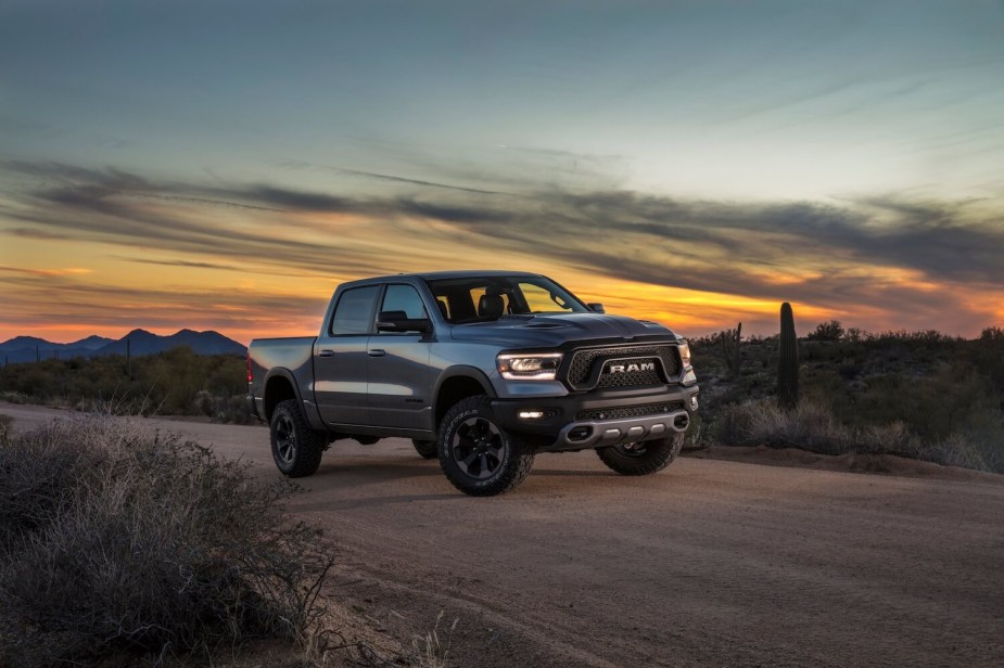 Gray Ram 1500 pickup truck parked on a dirt road, a desert sunset visible in the background.