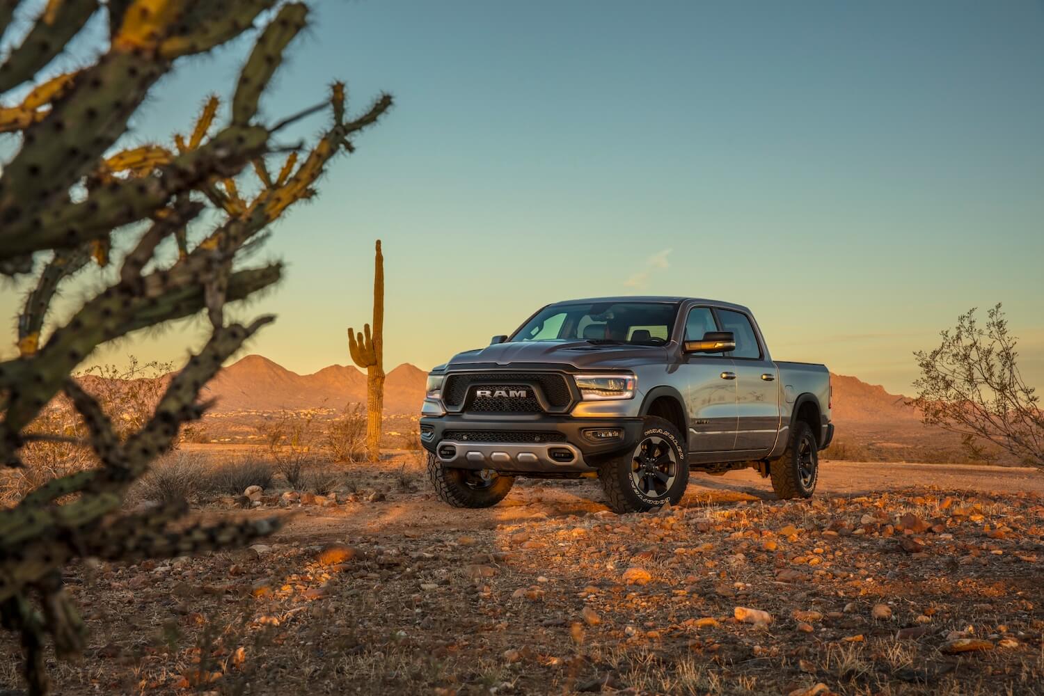 Silver 2023 Ram 1500 rebel parked in the desert, a sunset visible behind it.