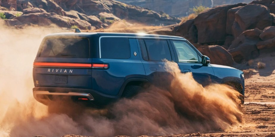 A blue 2023 Rivian R1S full-size SUV is driving off-road. 